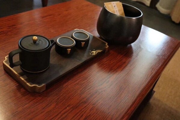 Una mesa de madera con una bandeja que contiene una tetera negra, dos tazas pequeñas y una taza negra.