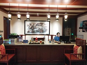 A reception desk with a large framed painting above it, a computer, and various items on the counter. - CQJ Lestay Hotel (Hangzhou)