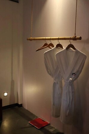 A hallway with a wooden rack holding white robes and a red object on the floor. - CQJ Lestay Hotel (Hangzhou)