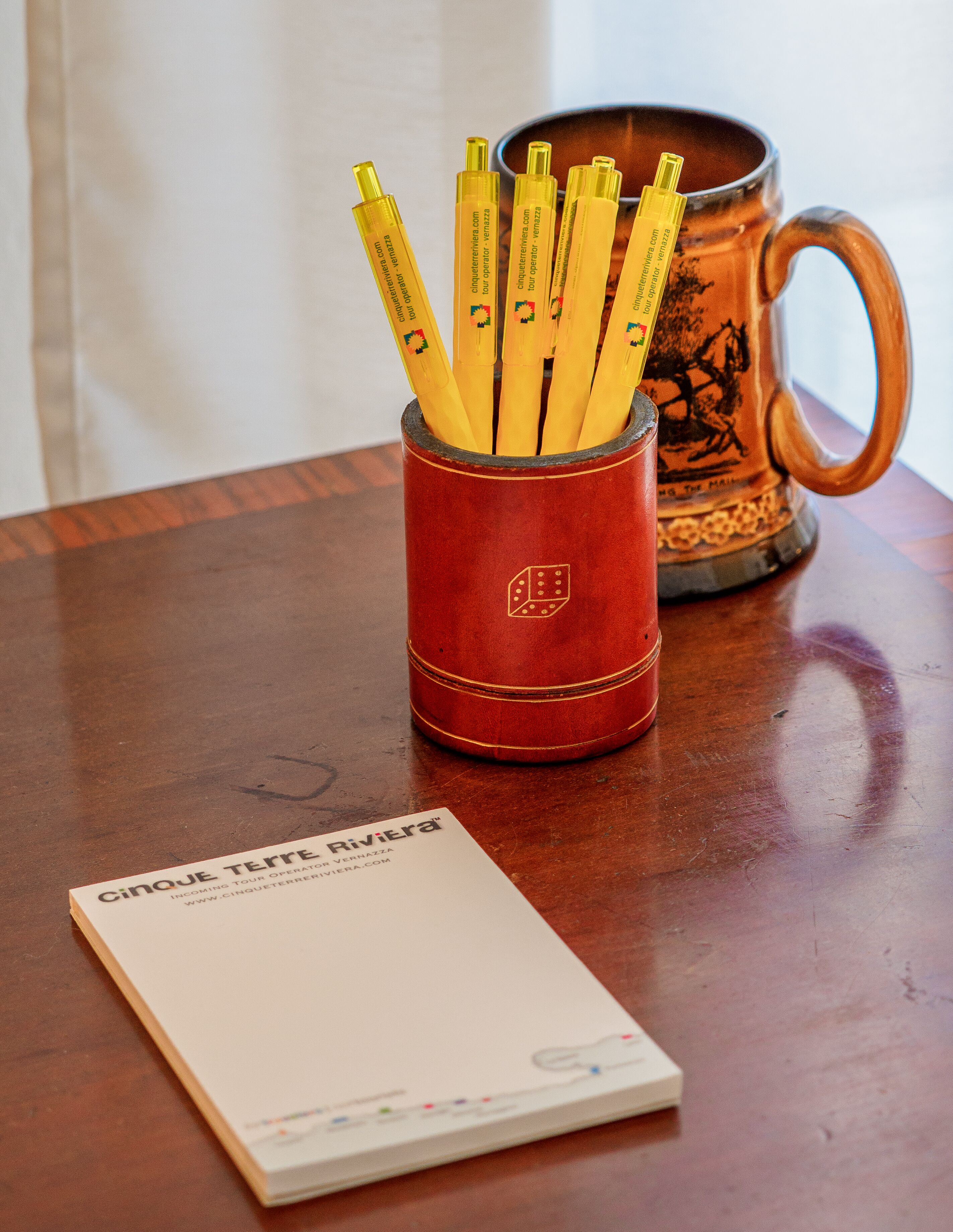 A red pencil holder with pencils, a mug, and a booklet on a wooden table.