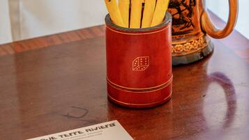 A red pencil holder with pencils, a mug, and a booklet on a wooden table.