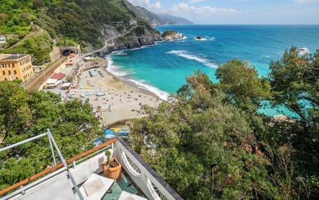 A coastal hotel with a beach view, a pool, and a mountain backdrop.