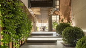 A modern building with a concrete pathway leading to a wooden fence and a dark panel wall. - Alkyon Hotel (Skiathos)