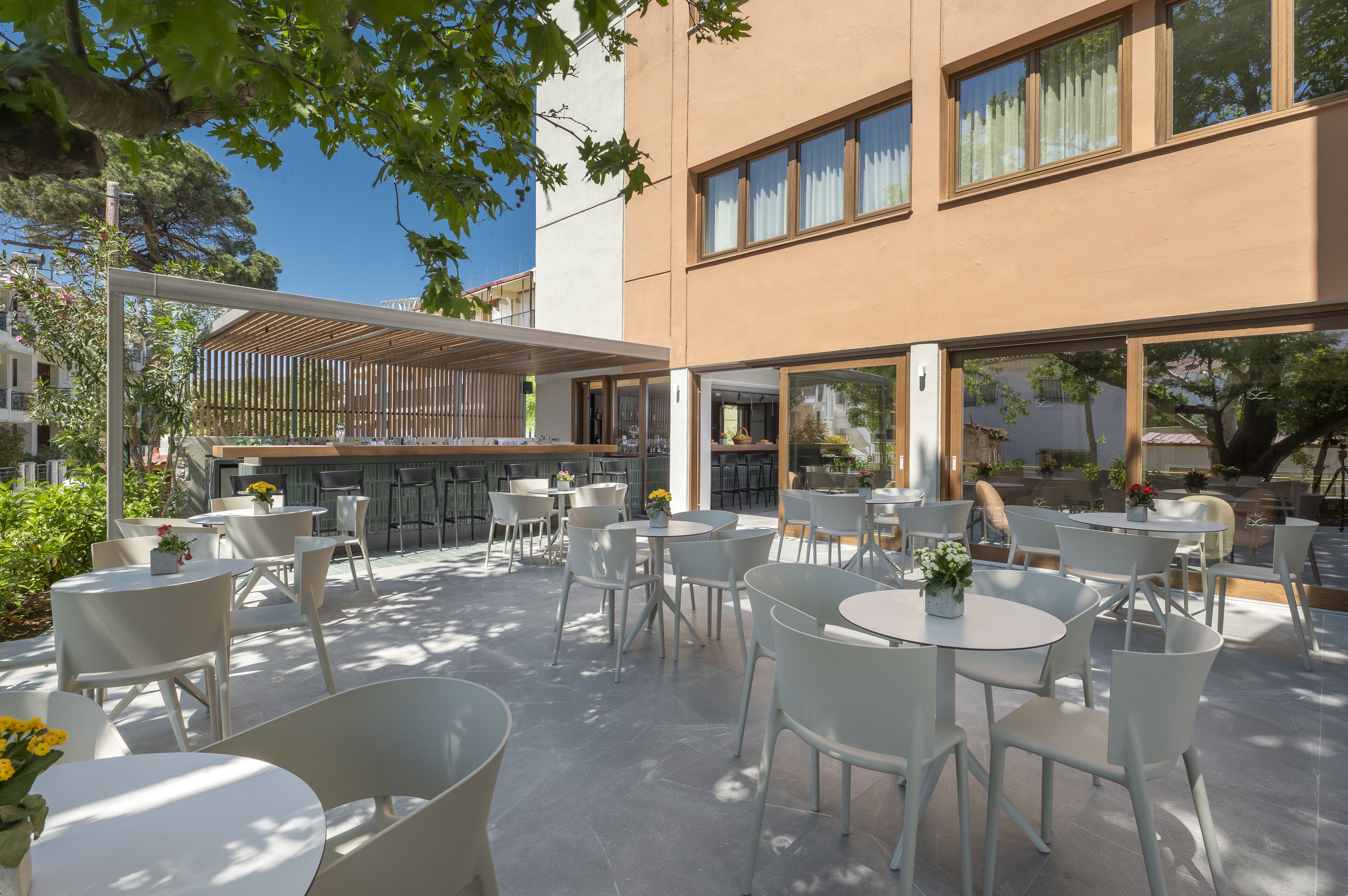 An outdoor seating area with round tables and chairs, a pergola, and a building with large windows.
