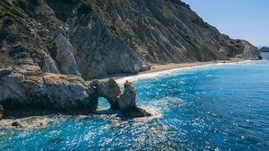 A coastal landscape with a rocky shoreline, clear blue sea, and a sandy beach. - Alkyon Hotel (Skiathos)
