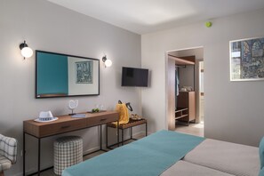 A modern hotel room with a bed, a desk with a chair, a television, and a wardrobe.