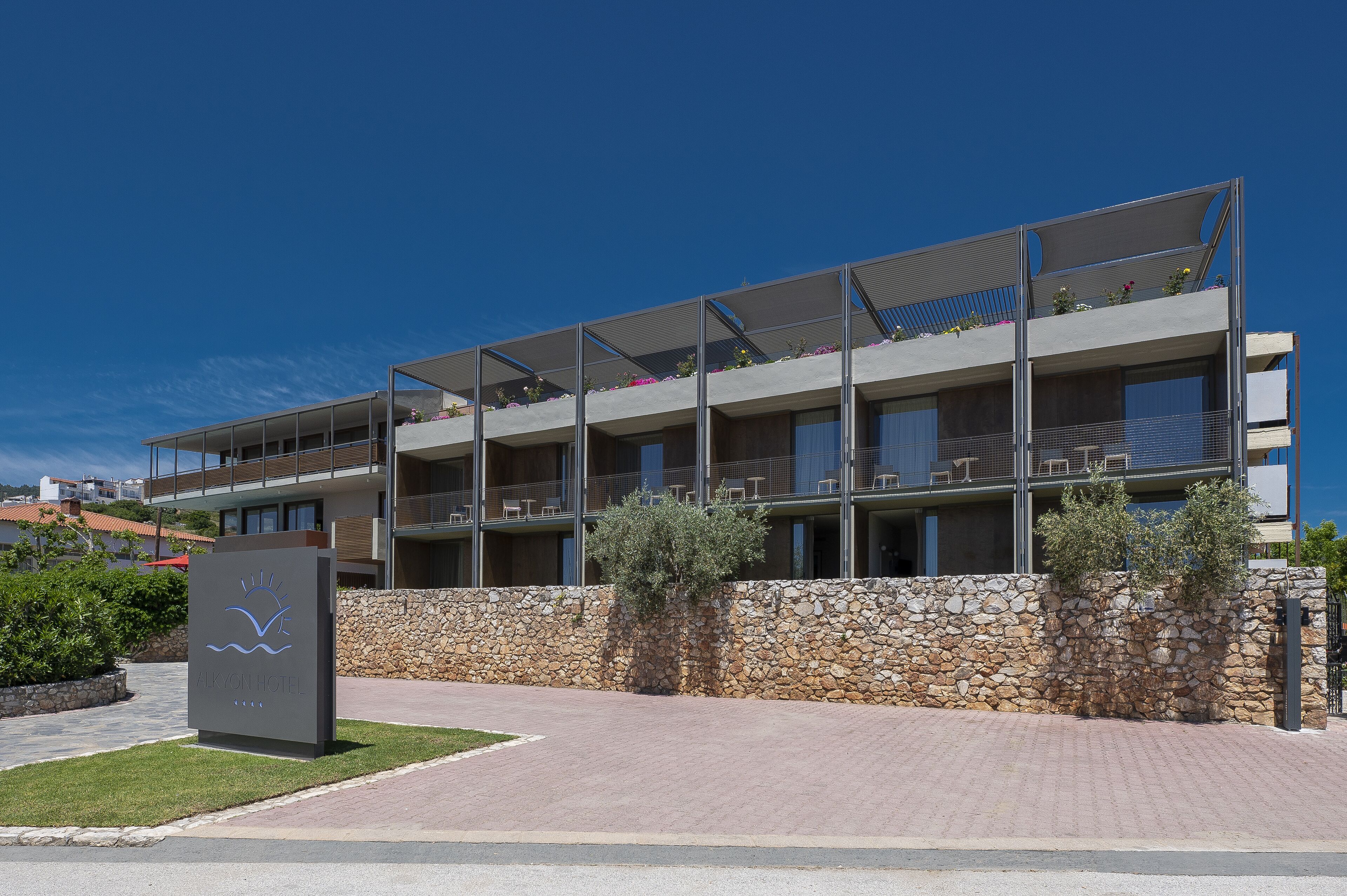 A modern hotel with a stone facade, multiple balconies, and a clear sky.