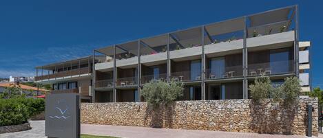 A modern hotel with a stone facade, multiple balconies, and a clear sky.