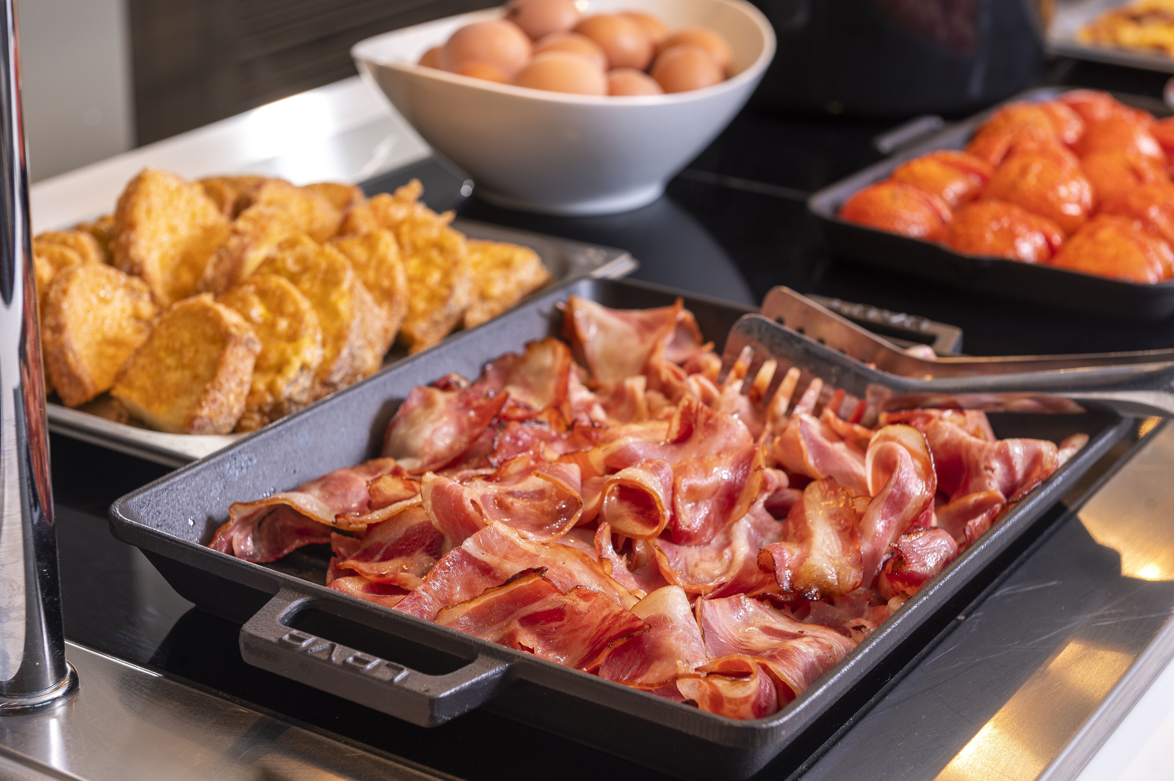 Un bufé de desayuno con tocino, huevos y rodajas de naranja.