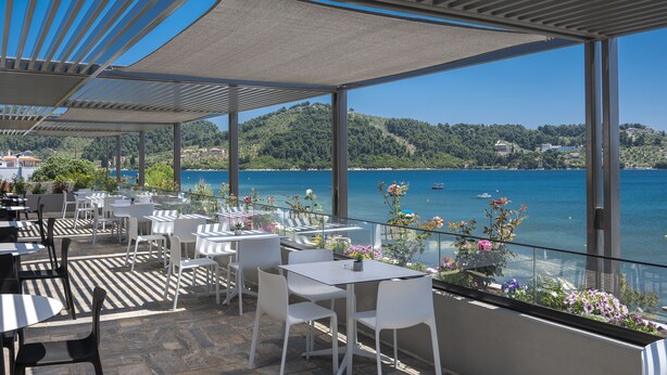 A terrace with tables and chairs overlooking a lake. - Alkyon Hotel (Skiathos)