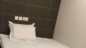 A neatly made bed with white bedding in a room with a dark tiled wall and a plain white ceiling. - Lam Shan Hotel (Kowloon)