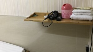 A wooden shelf with a hairdryer, a pink container, and folded towels. - Lam Shan Hotel (Kowloon)