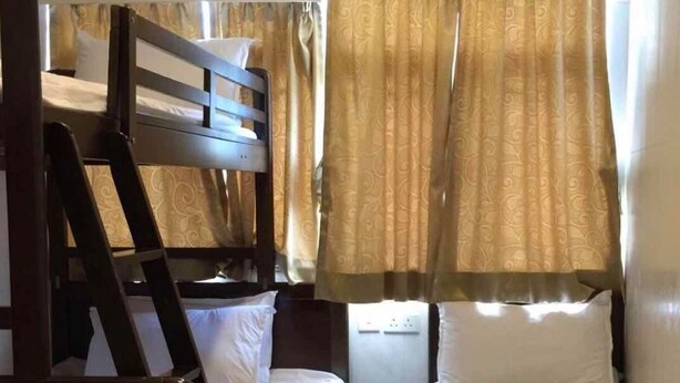 A compact room with two bunk beds and a single bed, featuring a patterned curtain and a window with natural light. - Lam Shan Hotel (Kowloon)