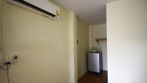 A room with a white air conditioner mounted on the wall, a small white refrigerator, and a power outlet with a phone charger plugged in. - Baan Chomlay Resort (Khanom)