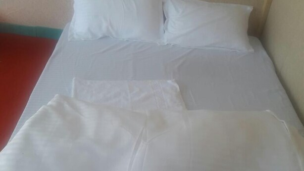 Ein Bett mit weißer Bettwäsche und Kissen, eine rote Wand und eine beige Decke.