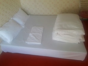 A neatly made bed with white linens and pillows, a red table beside it, and patterned wallpaper on the walls.