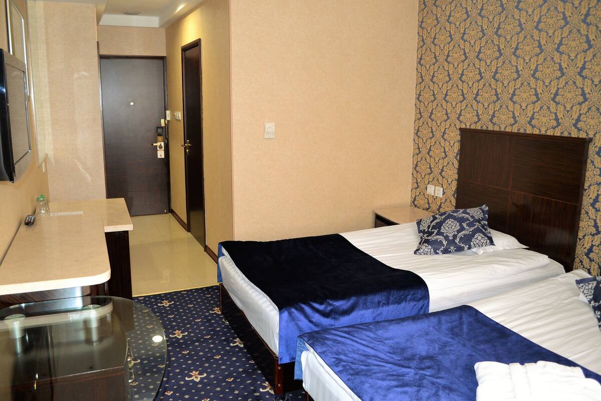 A hotel room with two beds, a desk, a mirror, and a patterned wall.