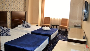 A hotel room with two beds, a small table, a TV, and a window with curtains. - Renion Hills Hotel (Almaty)