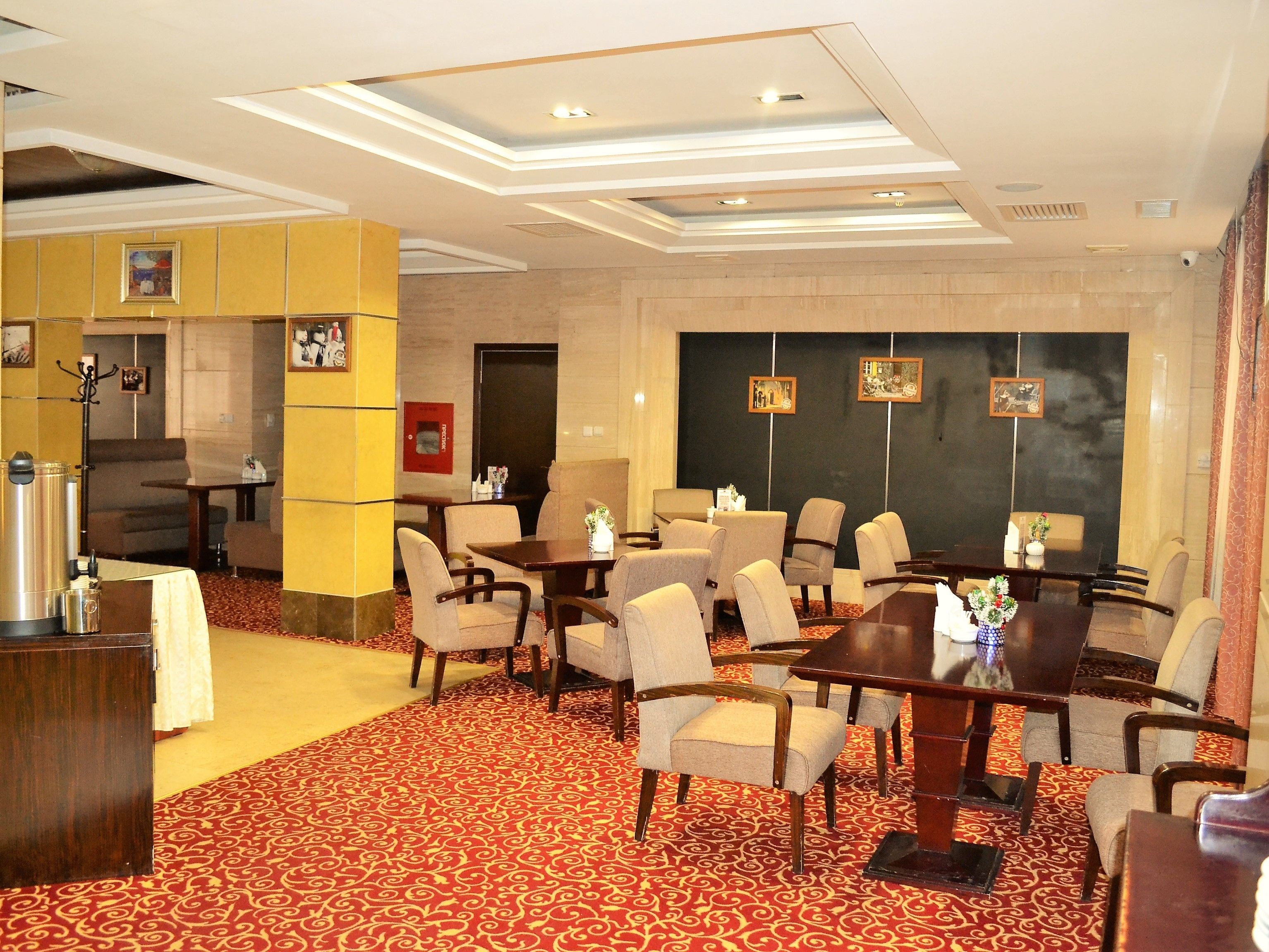 A hotel lobby with a red patterned carpet, multiple seating areas, and a large wall with framed pictures.