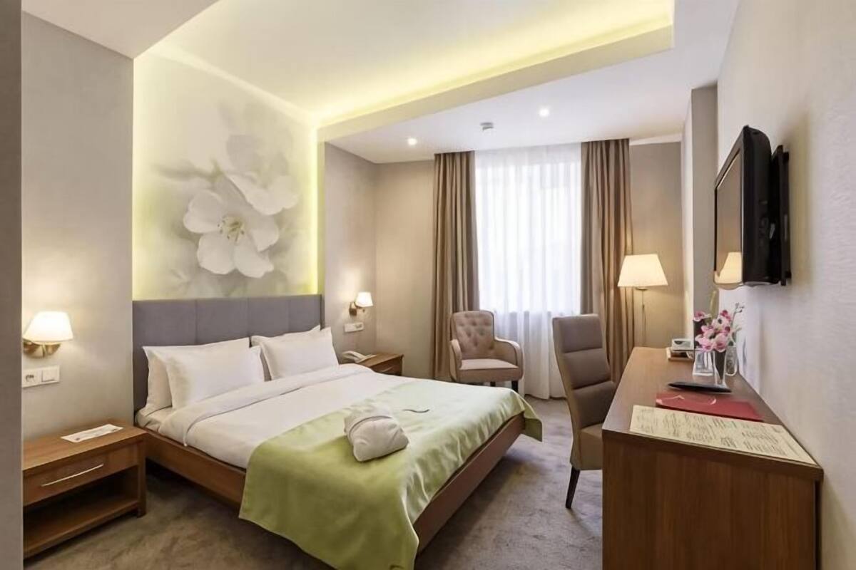 A hotel room with a bed, bedside tables, a desk, a chair, a TV, and a large flower wall decoration.