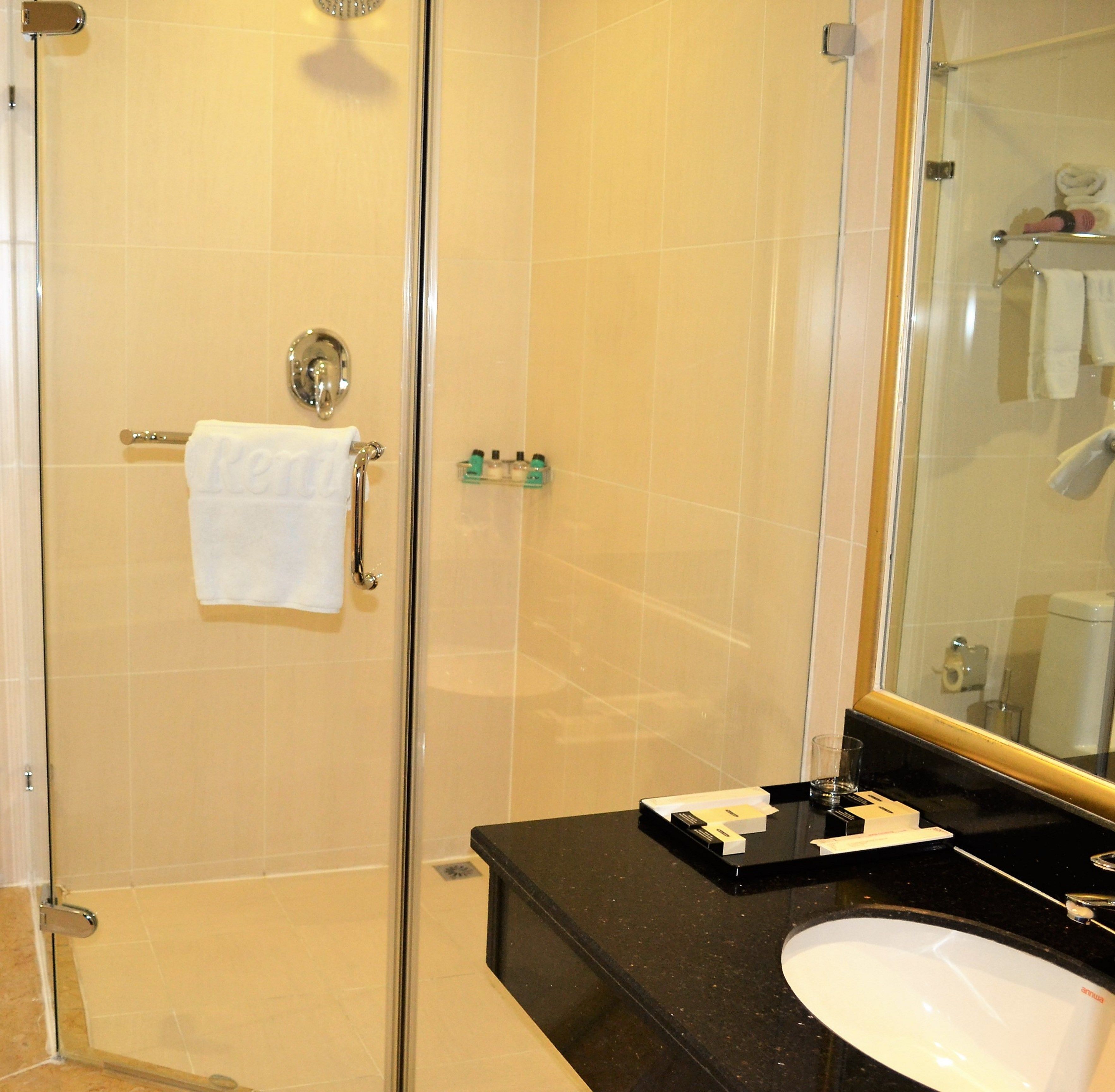 A hotel bathroom with a glass-enclosed shower, a black countertop, and a white sink.