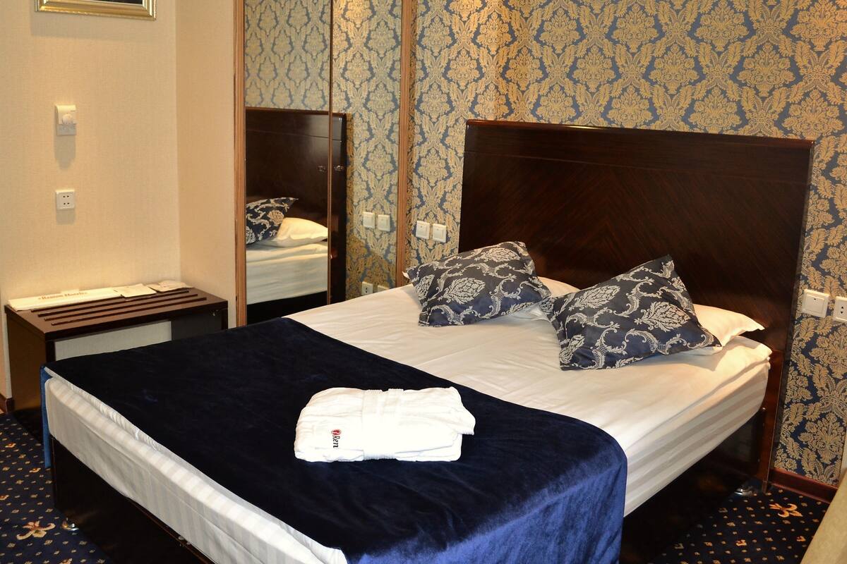 A hotel room with a large bed, a nightstand, a mirror, and patterned wallpaper.