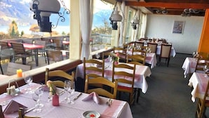 Un restaurant où les tables sont dressées pour le service, offrant une vue sur les montagnes grâce à de grandes fenêtres.