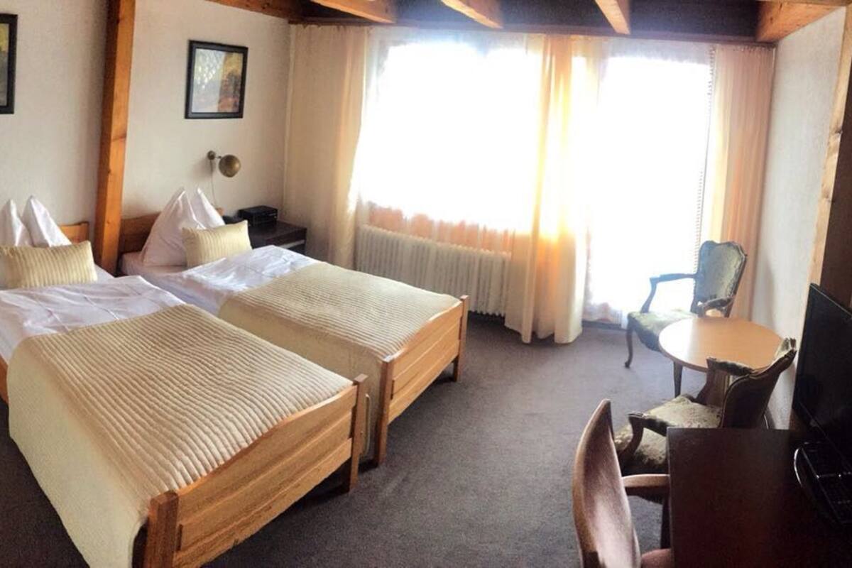 Habitación de hotel con dos camas individuales, un escritorio, una silla y un televisor.