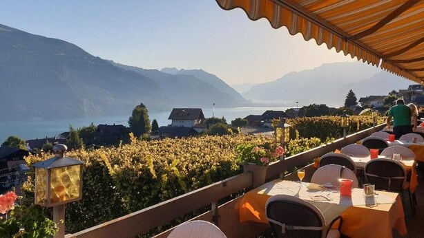 Une terrasse avec des tables et des chaises donnant sur un lac et des montagnes.