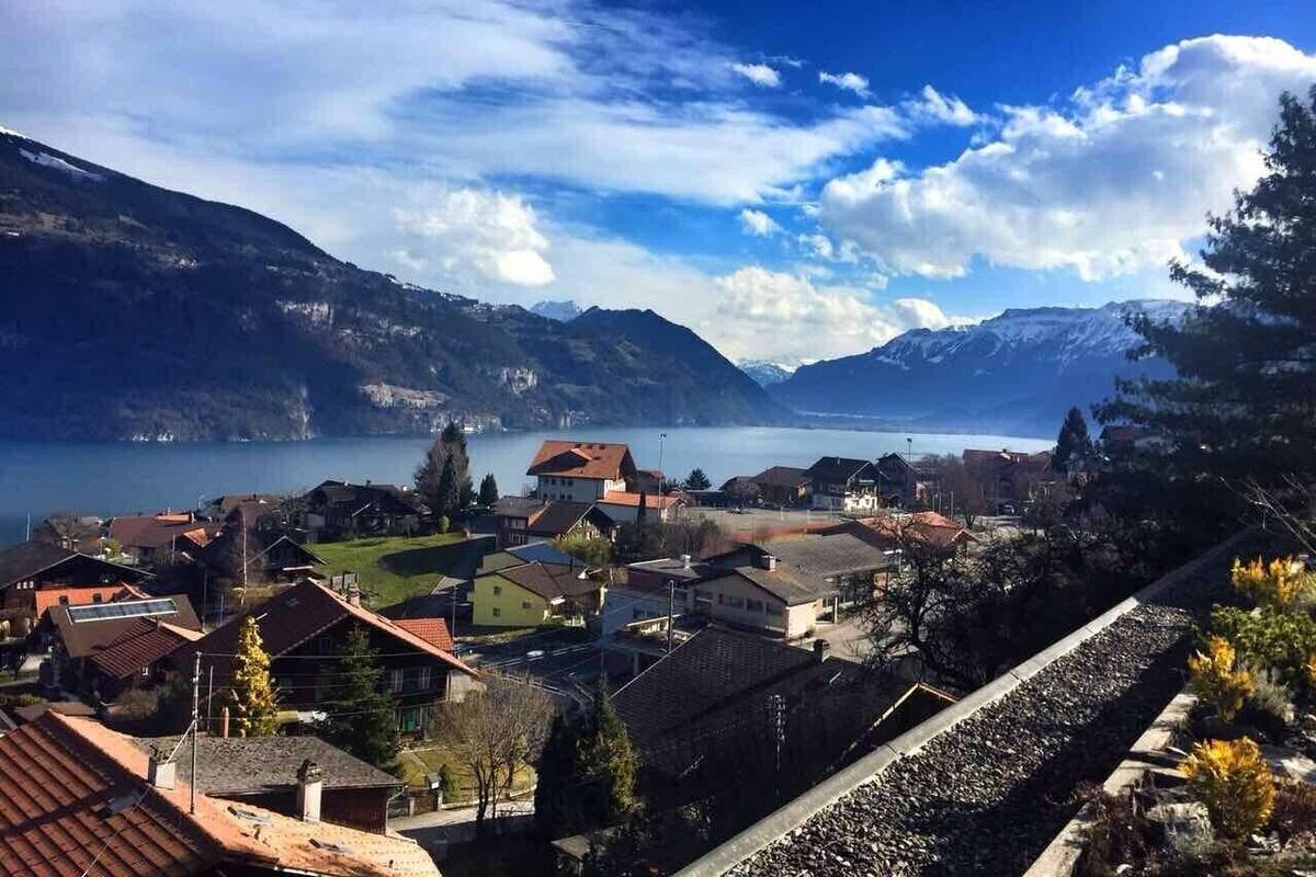 Un pueblo a orillas del lago con casas tradicionales, cielo despejado y montañas al fondo.