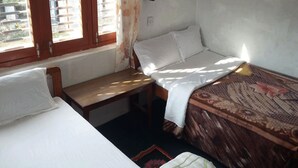 A small, simple room with two beds, a bench, and a window. - Galaxy Inn Guest House (Pokhara)