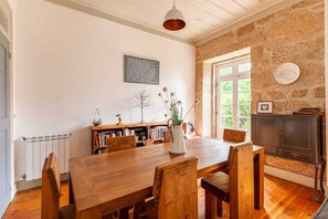 A dining area with a wooden table and chairs, a bookshelf, and a stone wall. - Casa do Cabeço (Tondela)