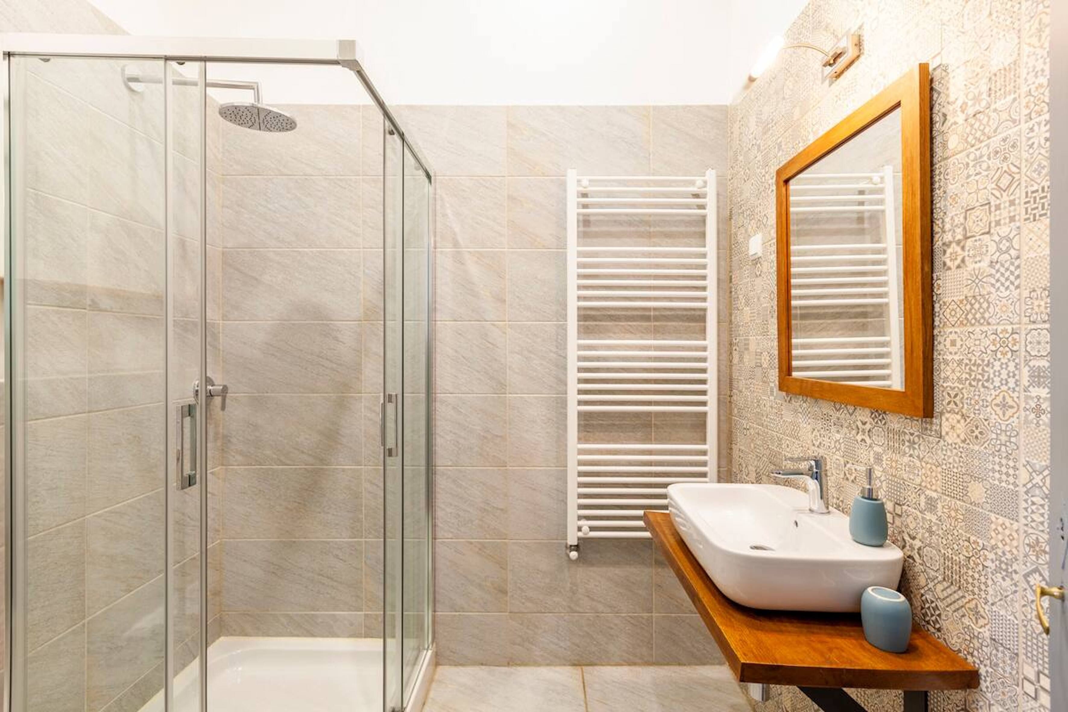 Een moderne badkamer met een douche met glazen wand, een wit wastafelmeubel met houten blad en decoratieve tegels op de muren.