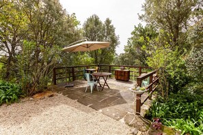 An outdoor patio with stone flooring, a table and chairs, a wooden deck, and surrounding greenery. - Casa do Cabeço (Tondela)