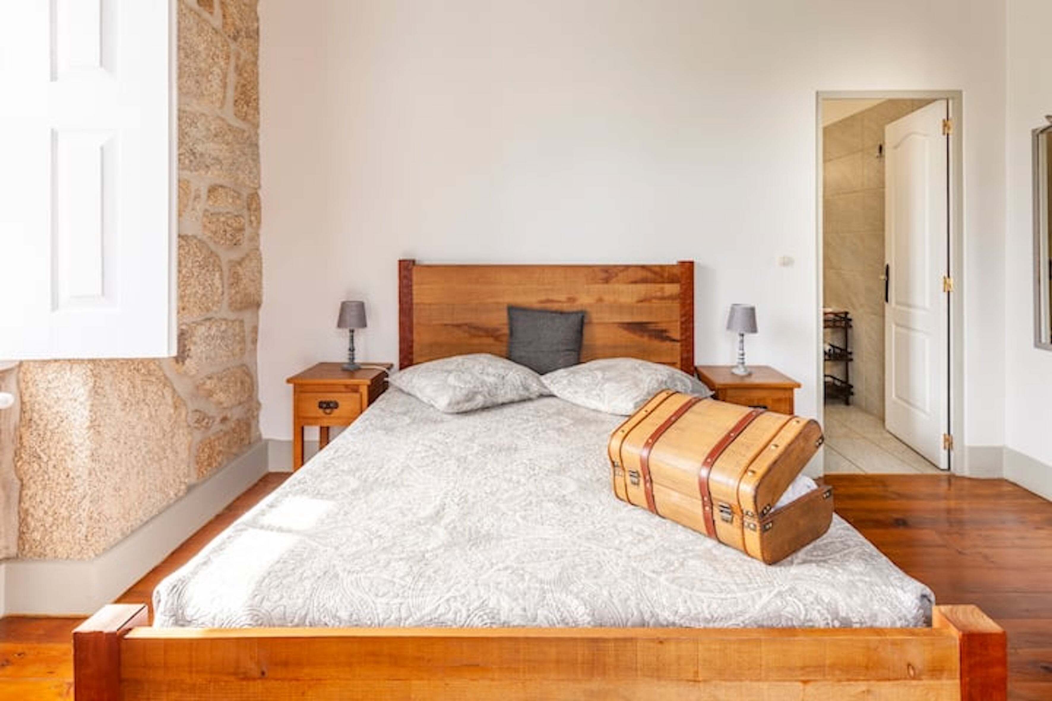 Un dormitorio con cama de madera, pared de piedra y una maleta sobre la cama.
