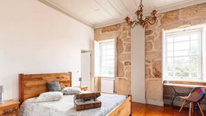 Un dormitorio con cama de madera, paredes de piedra, un escritorio y una silla junto a una ventana.