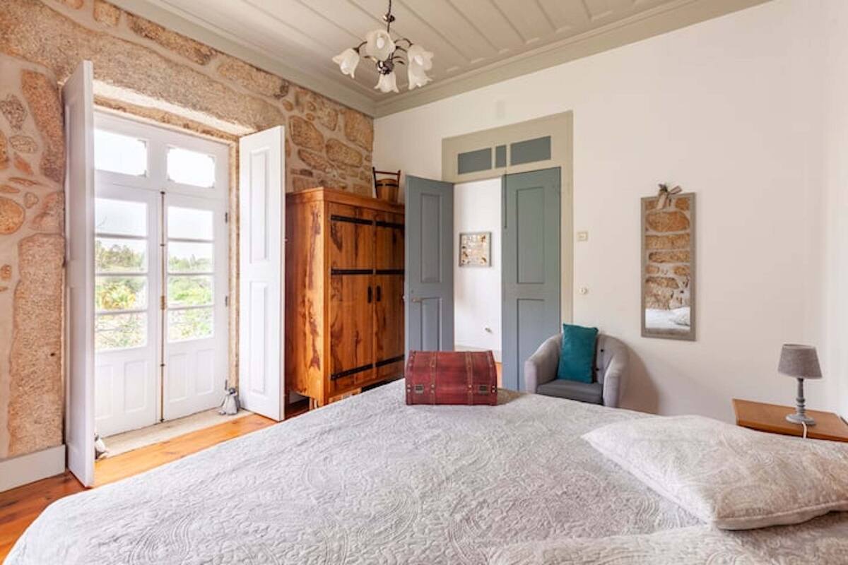 A bedroom with a large bed, a wooden wardrobe, a blue door, and a stone wall.