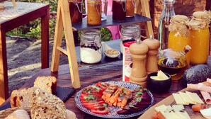 Una terraza de madera con diversos alimentos, entre ellos botes de conservas, una botella de aceite de oliva y un plato de verduras en rodajas.