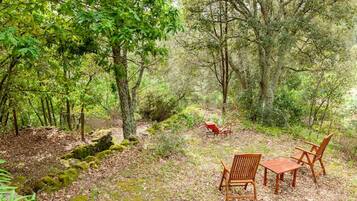 Un claro en el bosque con una mesa y sillas de madera, rodeado de árboles y un tractor rojo.