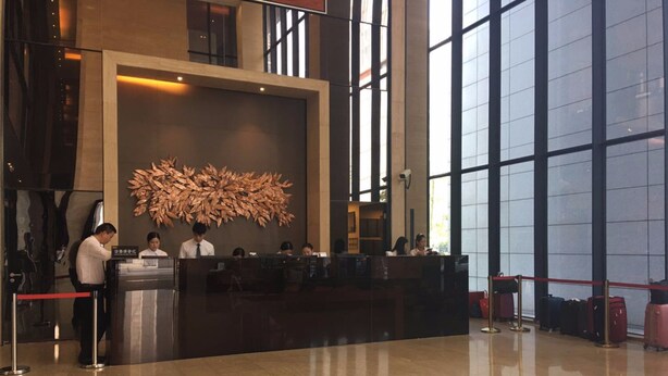 A reception area with a large desk, several staff members, and a decorative wall piece. - Checkinn Business Apartment-Poly World (Guangzhou)
