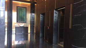 A modern lobby with a marble floor, a reception desk, and elevator doors marked with floor numbers. - Checkinn Business Apartment-Poly World (Guangzhou)