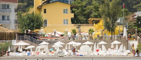 A coastal hotel with a poolside area, umbrellas, and a lifeguard tower.