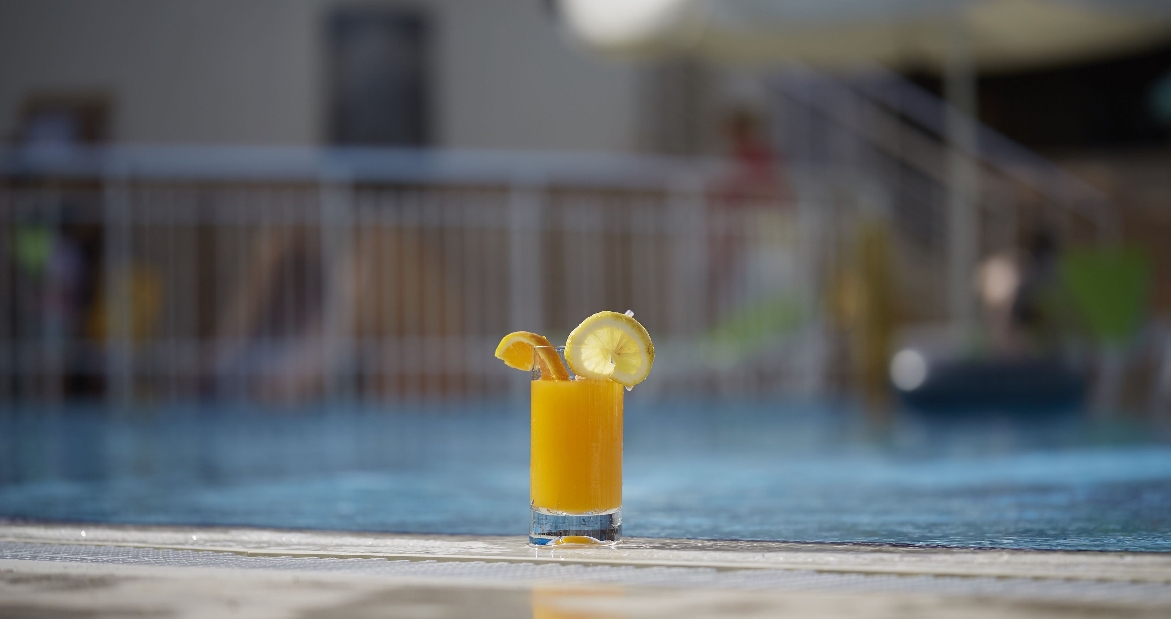 A glass of orange juice with lemon slices on a poolside table.