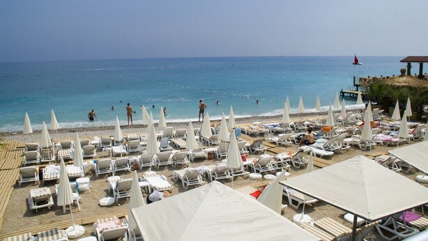 A beach with sun loungers and umbrellas, a pier with tables and a red sailboat, and the sea in the background. - Club Hotel Sunbel - All Inclusive (Kemer)