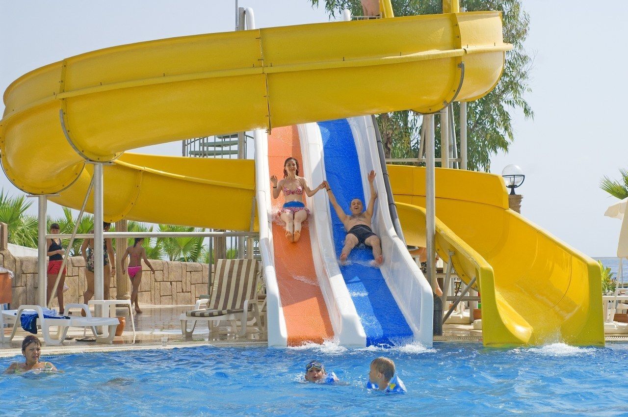 A water park with a large yellow water slide, a pool, and lounge chairs.