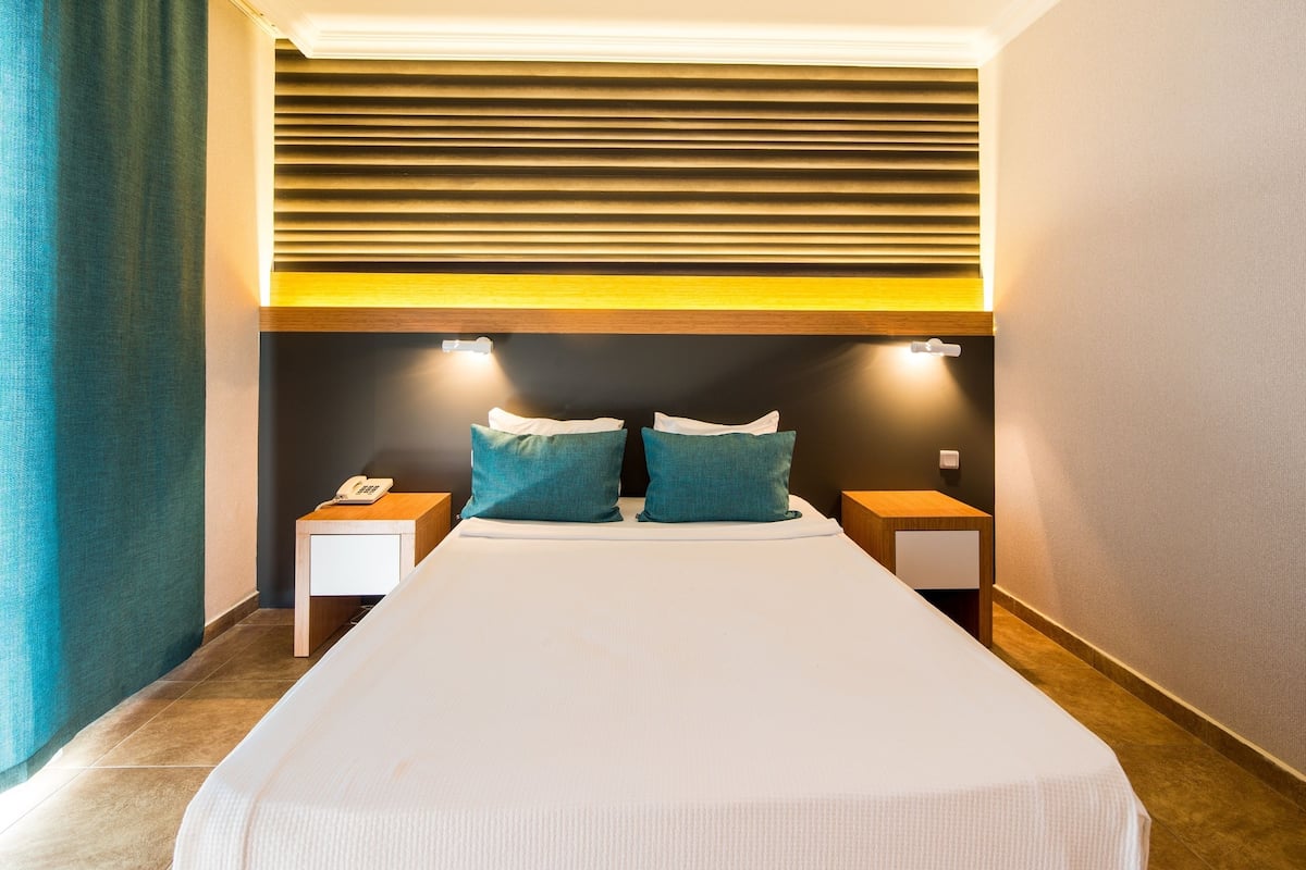 A hotel room with a large bed, two bedside tables, a telephone, and a wall-mounted light fixture.