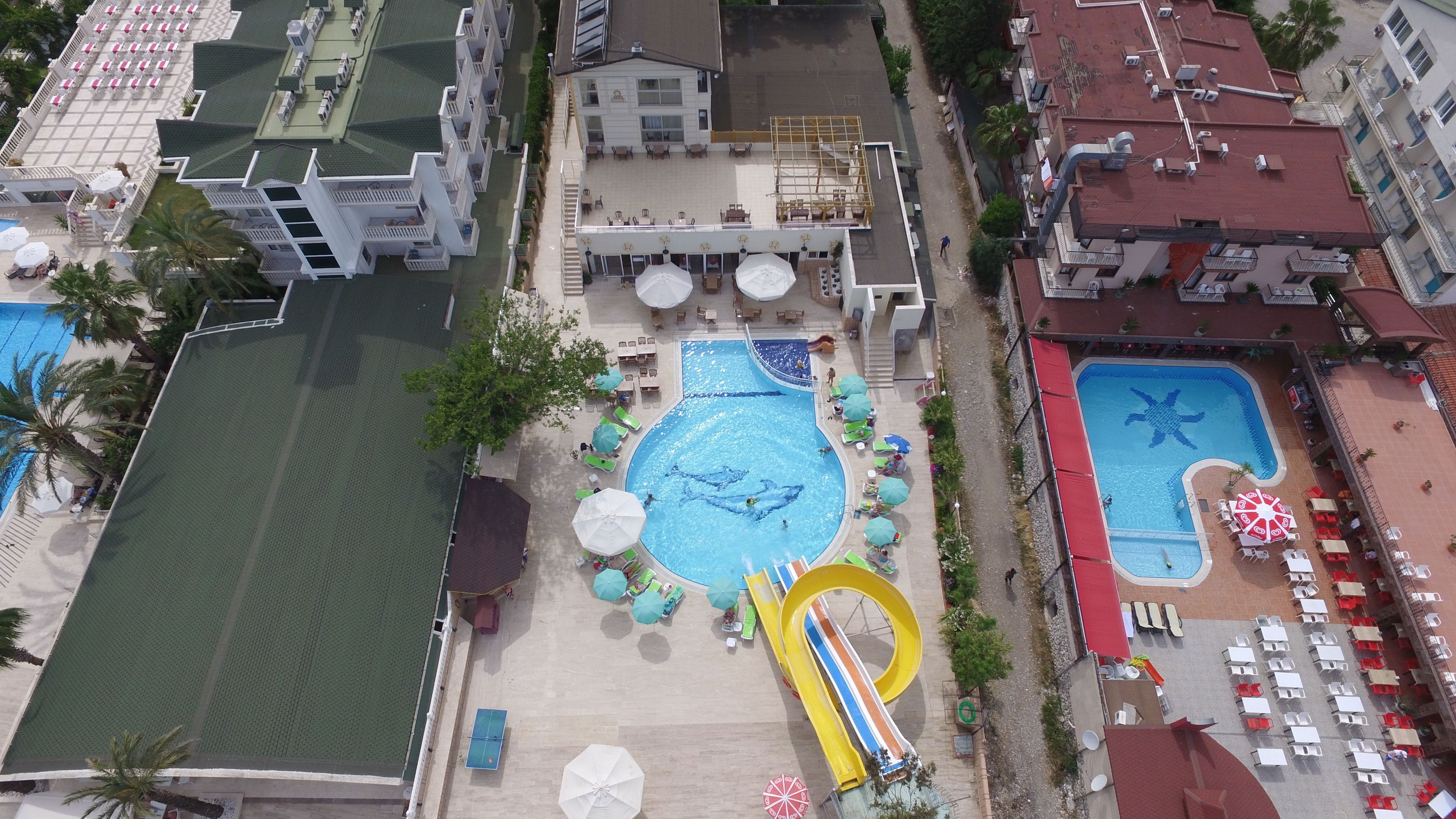 An aerial view of a hotel with multiple swimming pools, a water slide, and outdoor seating areas.