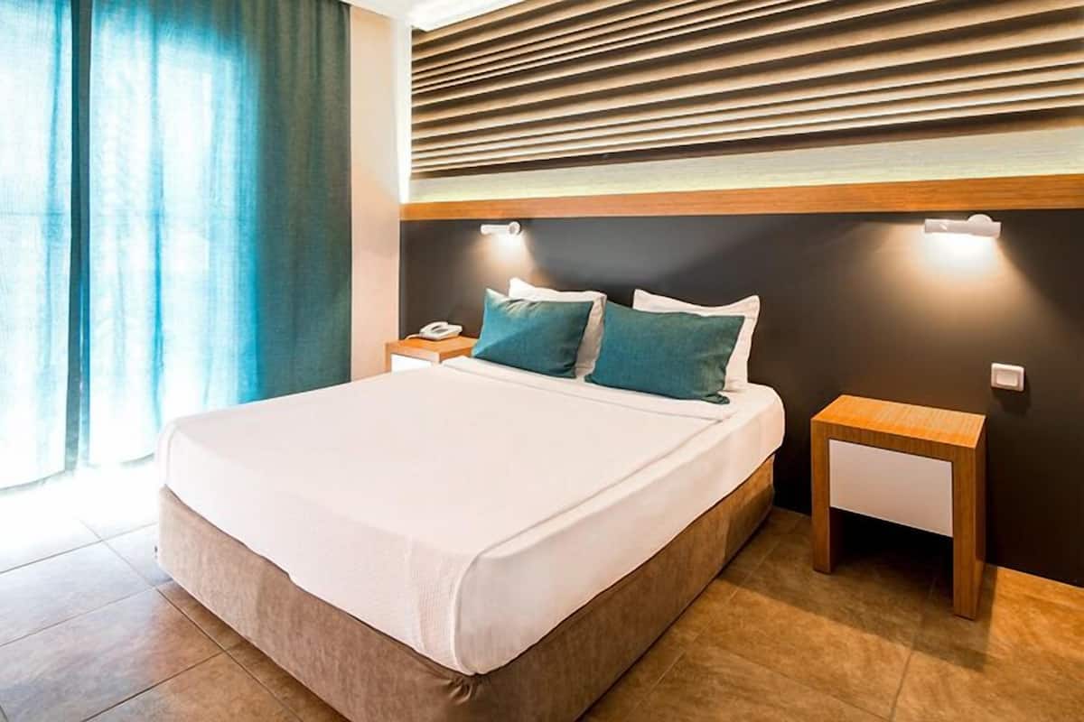 A modern hotel room with a large bed, two bedside tables, a nightstand, and a window with curtains.