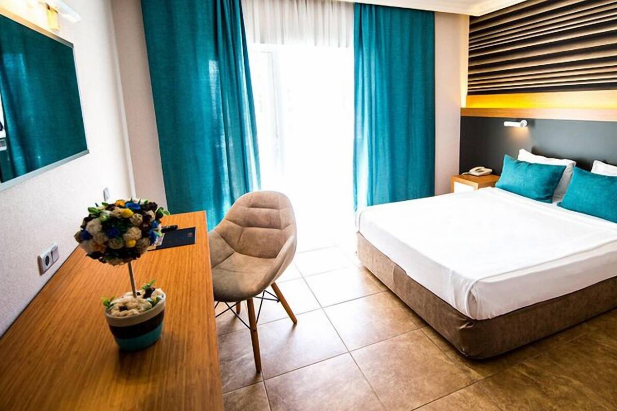 A hotel room with a bed, a chair, a desk, and a wall-mounted TV.