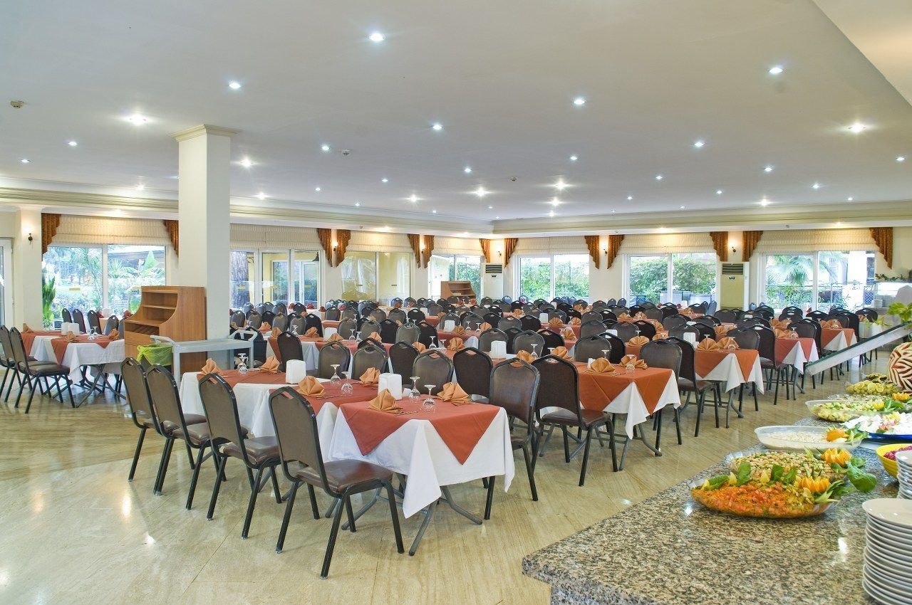 A large banquet hall with rows of tables and chairs, large windows, and a buffet area.